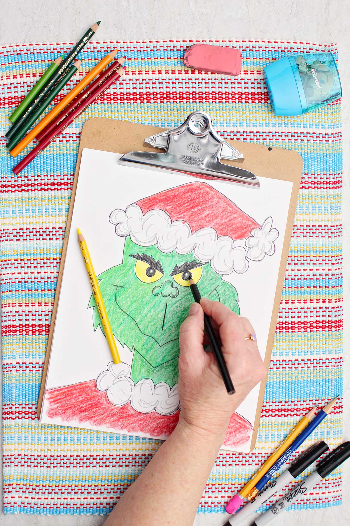 Person coloring in the Grinch pupils black on a colored in version of a Grinch sketch.