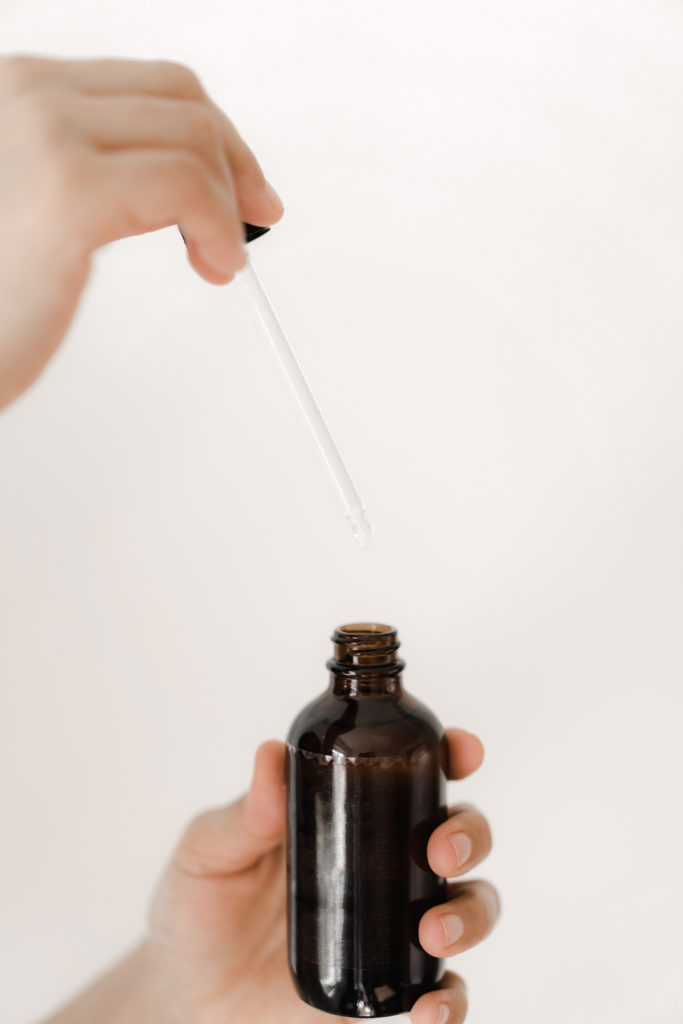 Hand holding a glass bottle and dropper.