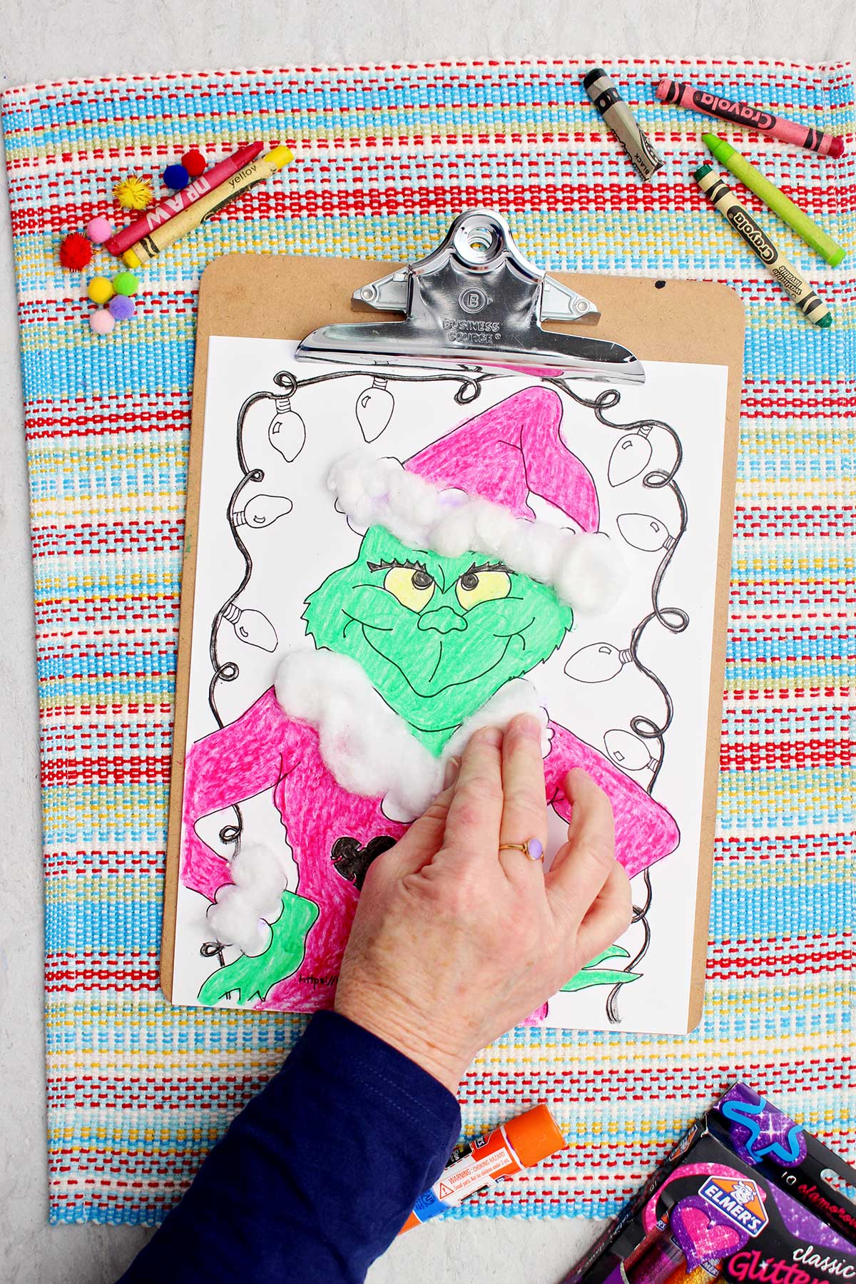 Person pressing cotton balls on accents on Santa coat on Grinch coloring page.