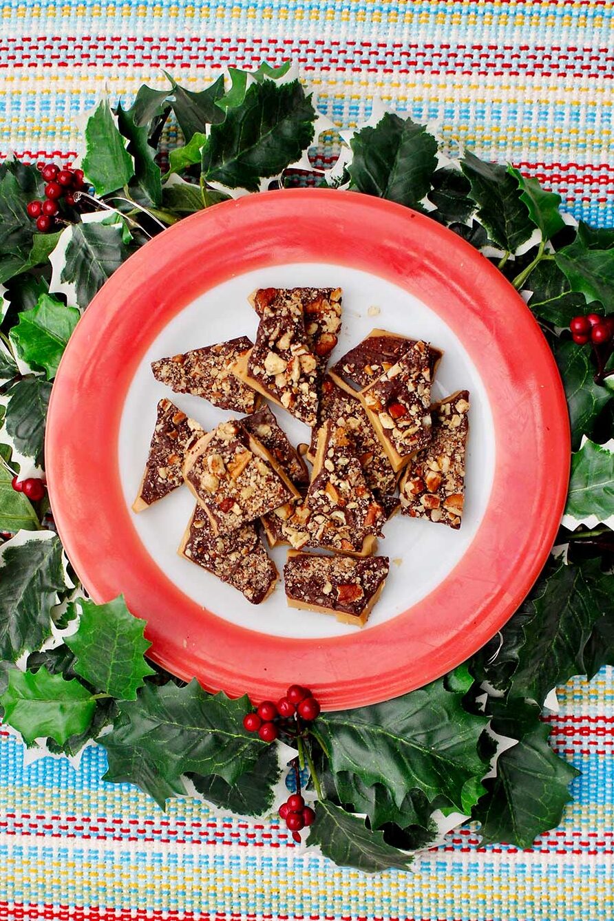 Red rimmed plate of English toffee with festive ivy surrounding it.