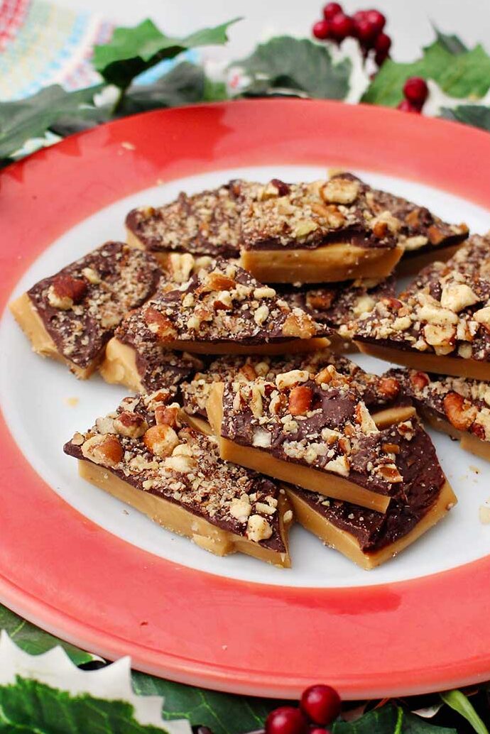 Red rimmed plate of English toffee with festive ivy surrounding it.