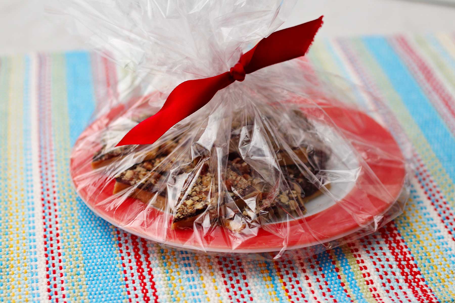 Plate wrapped in clear wrapping with red bow for gifting.