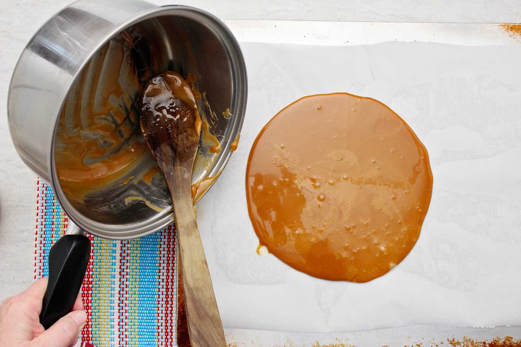 Person pouring toffee mixture on parchment paper.