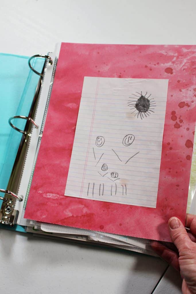 A child's pencil drawing of a family and sun on a page in a binder.