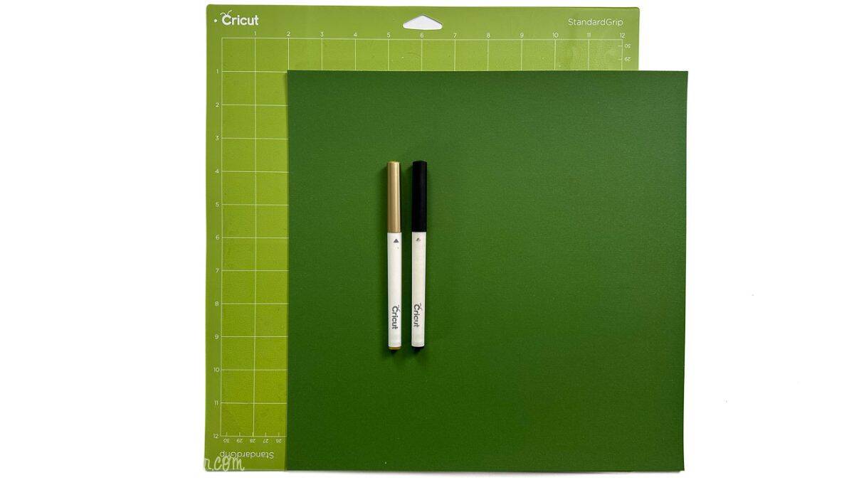 Cricut StandardGrip cutting mat with cardstock and two Cricut pens placed on top, showing supplies used to make DIY baby shower game tags.