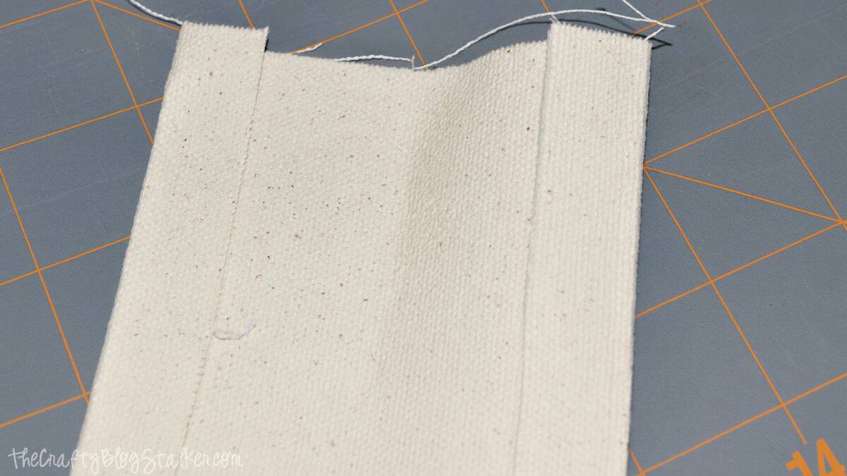 Close-up of folded canvas strap with pressed edges and stitched seams while making a handmade tote bag strap.