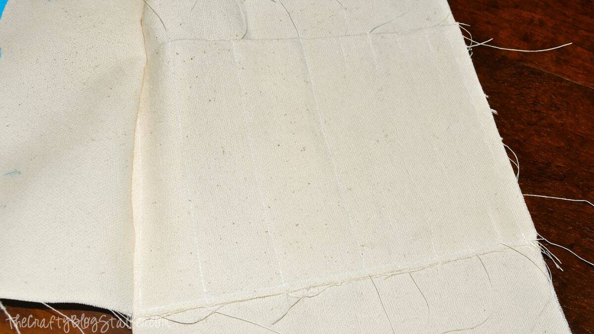 Canvas fabric piece with stitched vertical lines forming narrow pockets for holding crochet hooks in a handmade yarn tote bag.