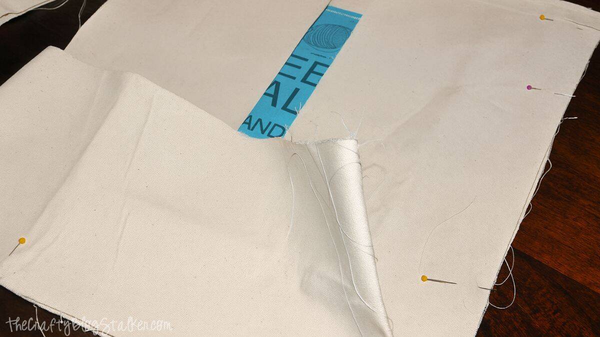 Canvas tote bag panels pinned together along the sides and bottom while assembling a yarn project bag.