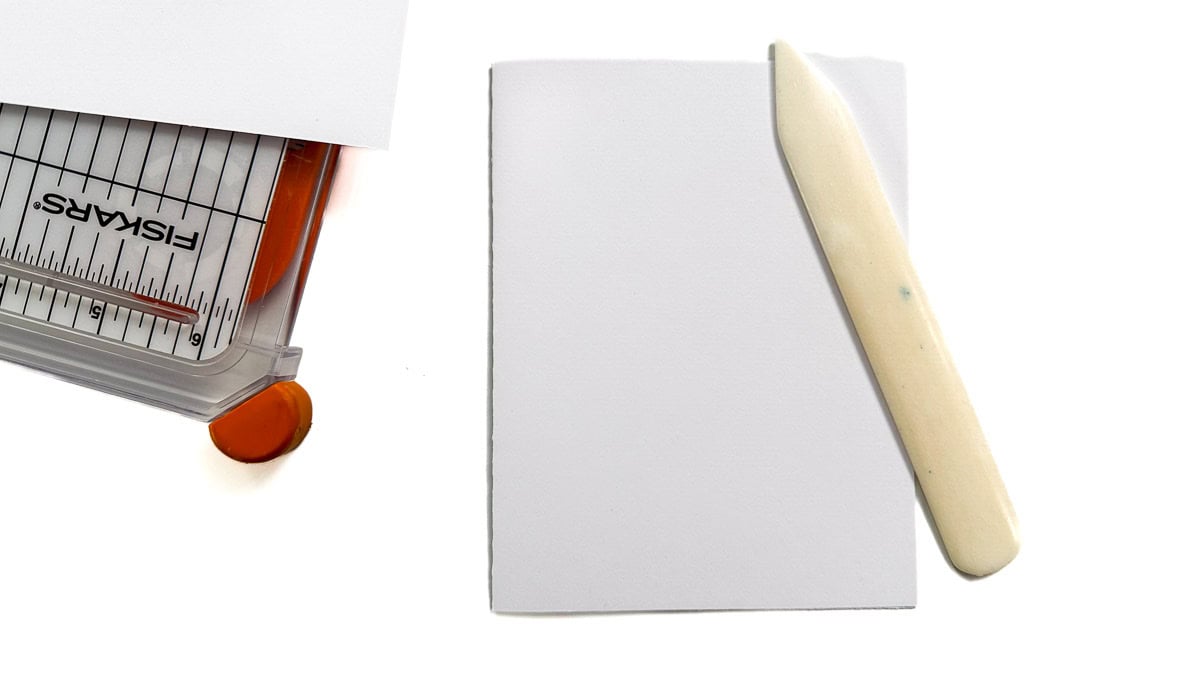 A2 folded card base on a white surface with a bone folder and paper trimmer partially visible.