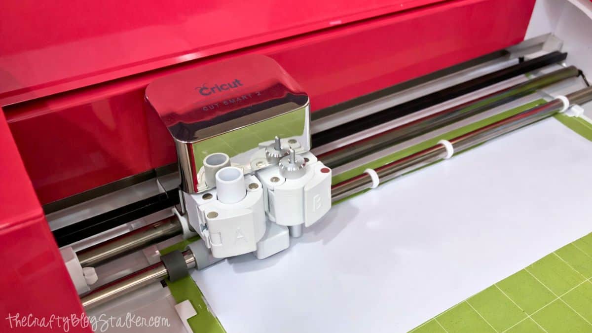 Cricut cutting machine with the blade carriage positioned over a cutting mat, ready to cut a sheet of material for a craft project.