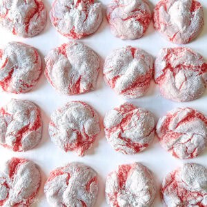 Pink lemonade crinkle cookies baked with cracked tops and a powdered sugar coating, arranged closely together on a flat surface.