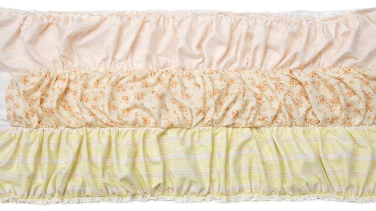 Three ruffled fabric strips sewn together in rows, showing gathered seams and patterned cotton pieces laid flat for a doll quilt top.