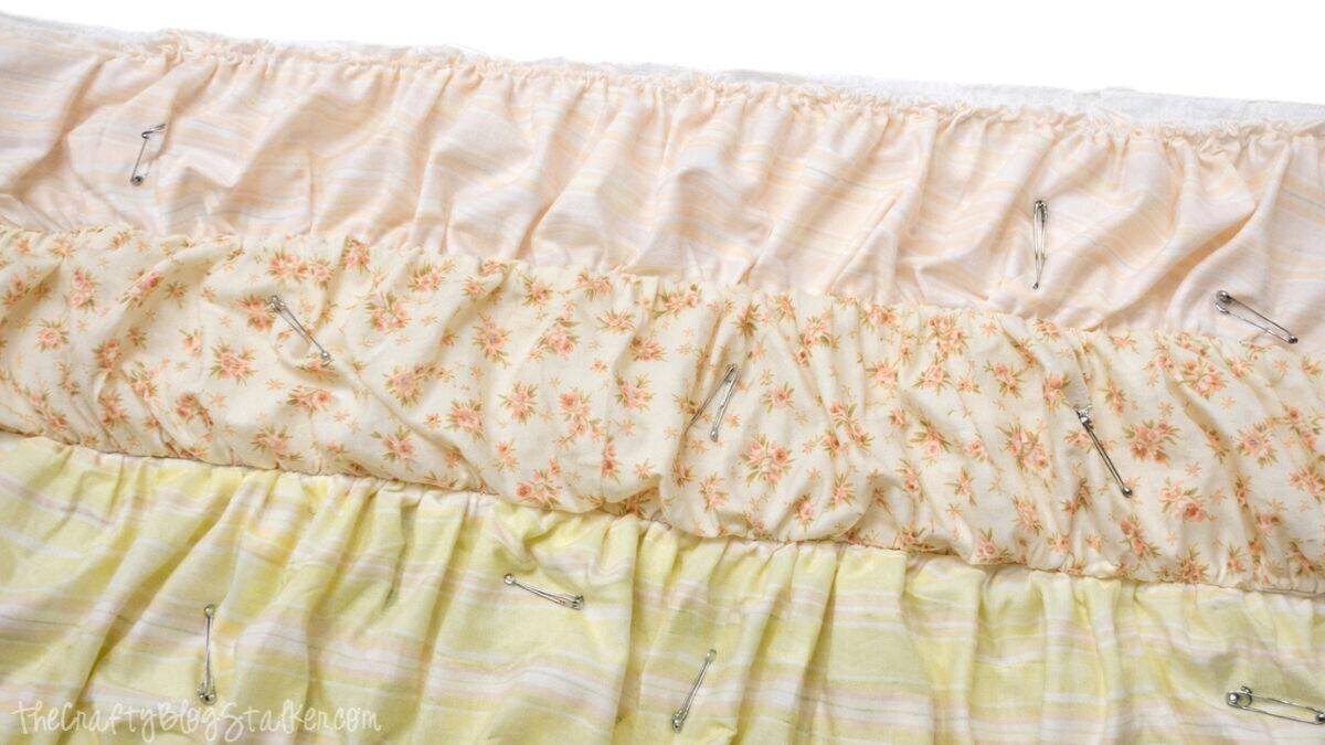 Ruffled quilt top layers pinned together with safety pins, showing gathered fabric strips secured in place before sewing.