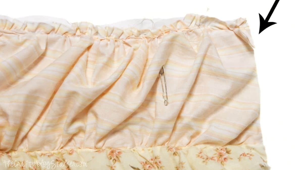 Close-up of ruffled quilt fabric with excess batting and backing extending past the edge, showing where layers will be trimmed before finishing.