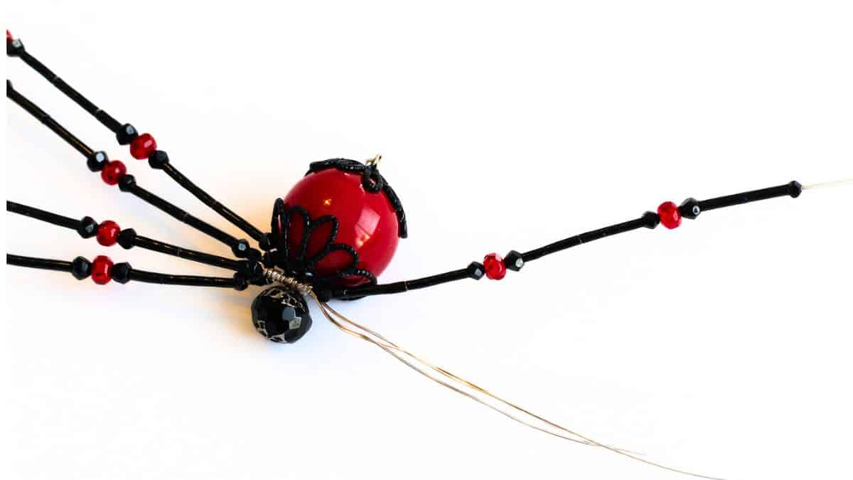 Beaded spider craft in progress with one wire leg being threaded with beads, showing the next step in assembling the spider legs.