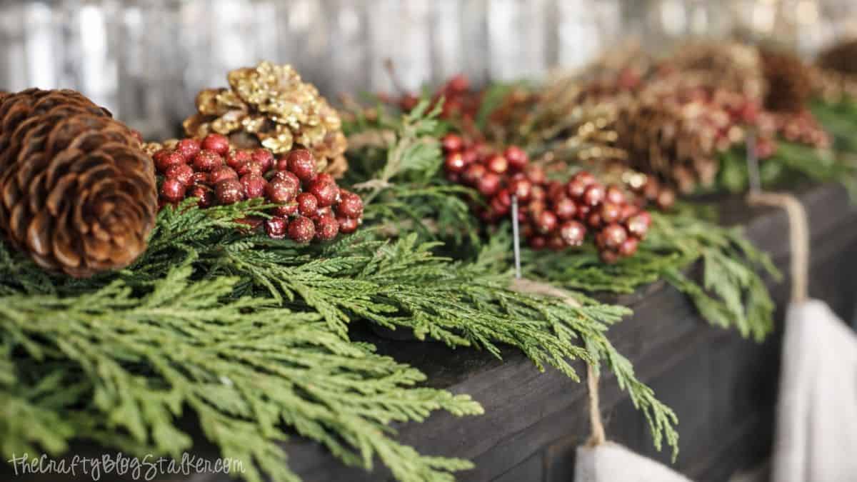 Close-up of cedar garland with pinecones and berry accents arranged along the top of a piano as part of Christmas mantel decor.