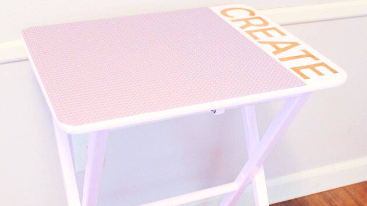 Portable DIY LEGO table with folding legs and a studded baseplate tabletop, designed for kids to build and play, shown set up against a wall indoors.