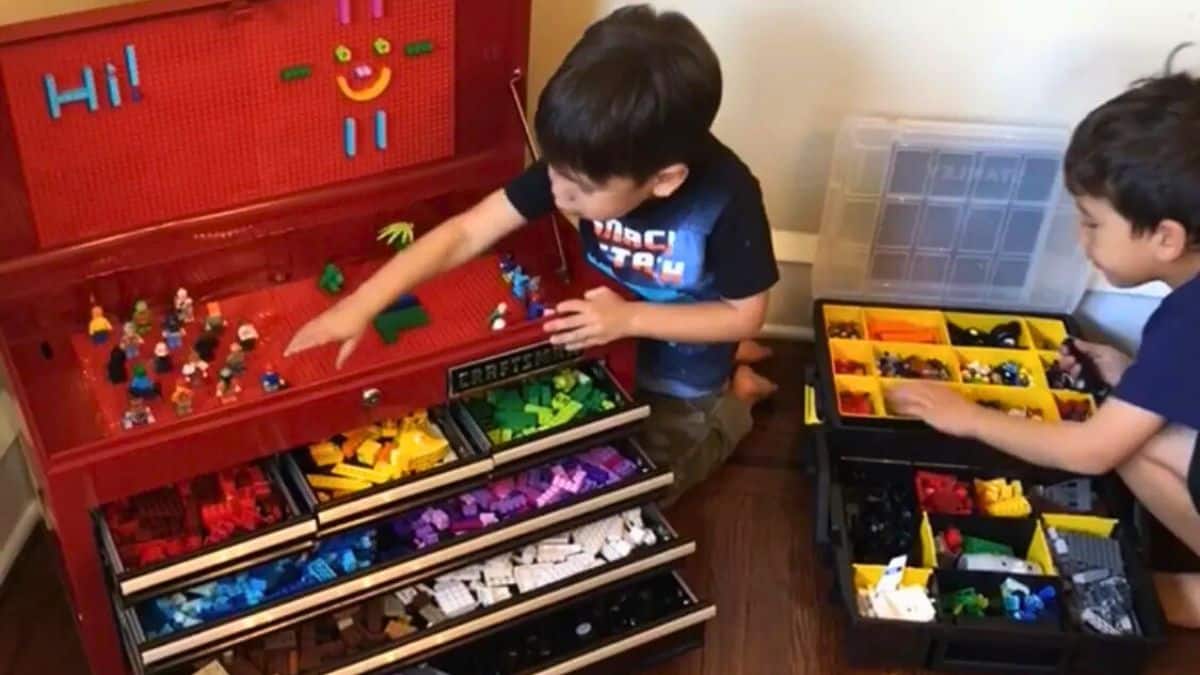 Two children sorting and playing with LEGO bricks using a repurposed tool chest with labeled drawers and compartment organizers for LEGO storage.