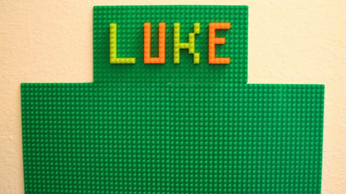 DIY LEGO wall made from connected base plates with LEGO bricks arranged to spell the name “Luke” at the top.