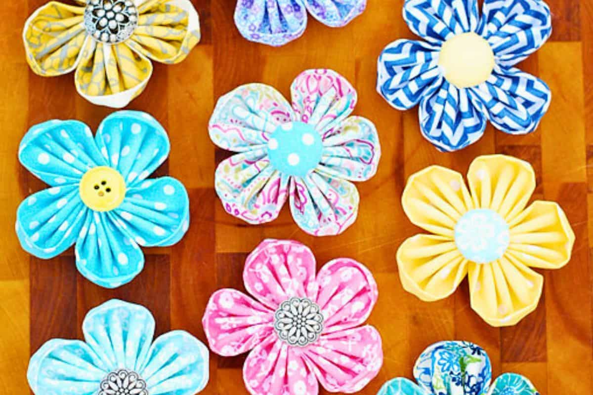 Assorted handmade round petal kanzashi fabric flowers with button centers, arranged in a flat lay on a wooden surface as a DIY craft example.