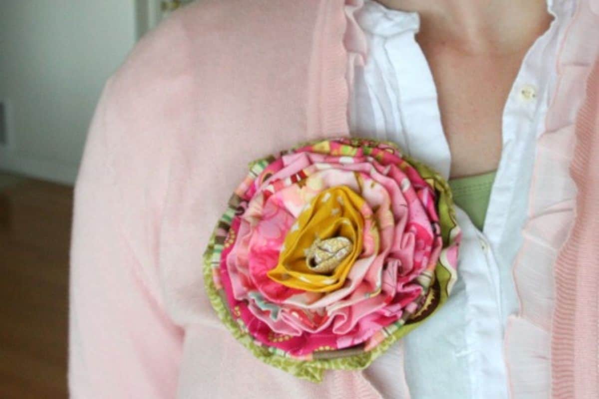 Handmade layered fabric flower brooch pinned to a cardigan, created from patterned fabric strips with a folded fabric center.