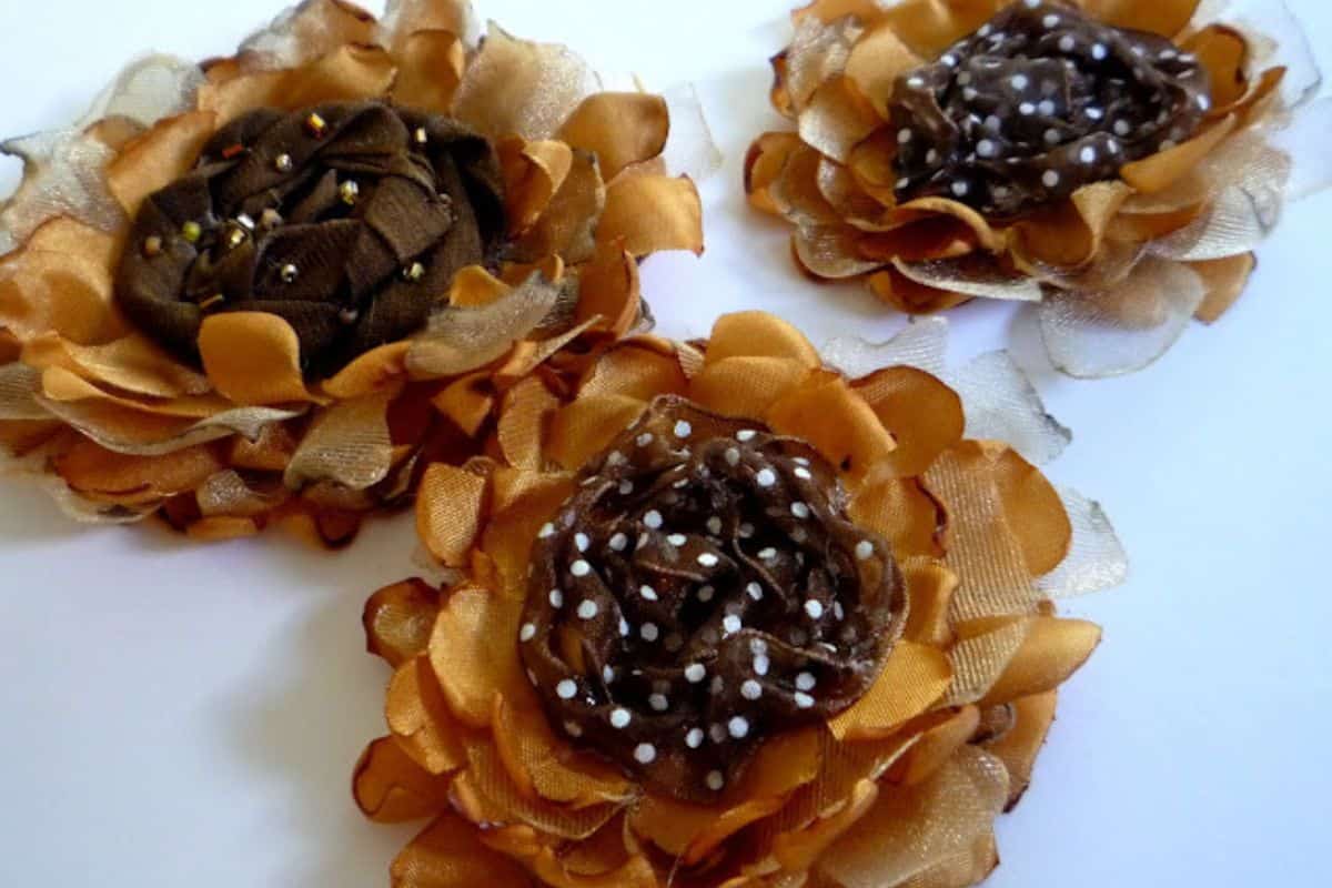 Three handmade fabric sunflowers with layered fabric petals and textured centers, arranged closely together on a white background as a craft project.