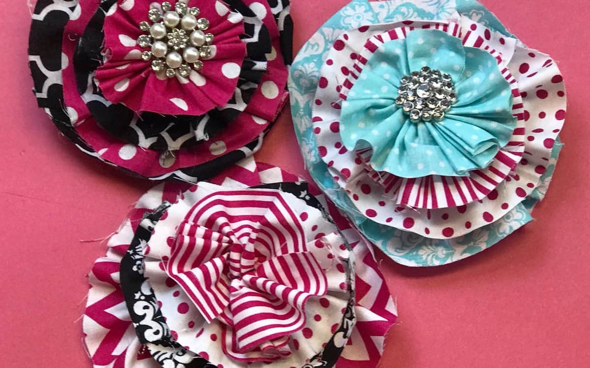 Three layered handmade fabric flowers with patterned petals and rhinestone-style centers, arranged on a flat surface as a DIY craft example.