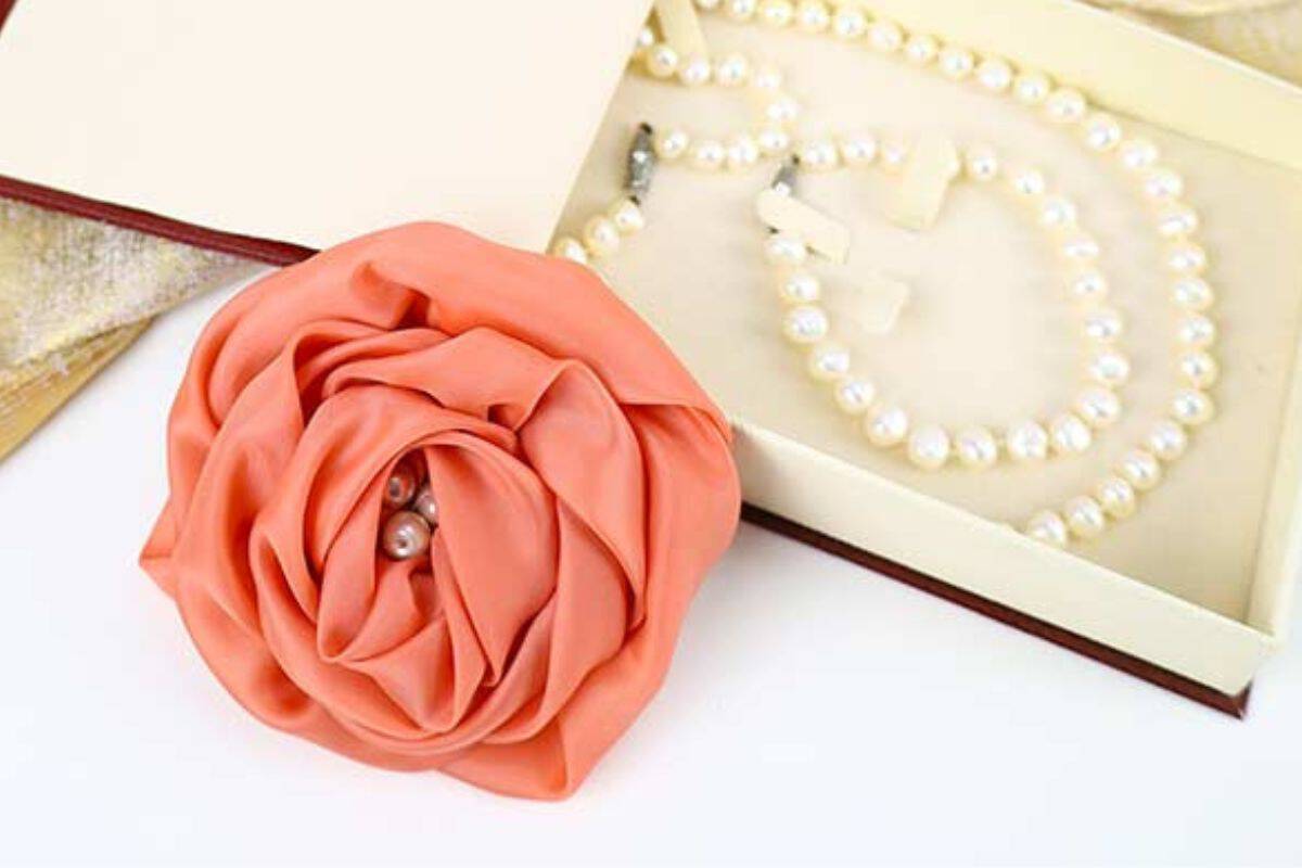 Handmade fabric rose with layered petals and pearl accents resting beside an open jewelry box containing a pearl necklace and earrings.