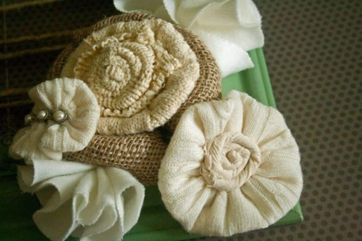 Handmade fabric flowers made from burlap and sweater material, layered and arranged as rustic floral decorations on a wrapped gift.