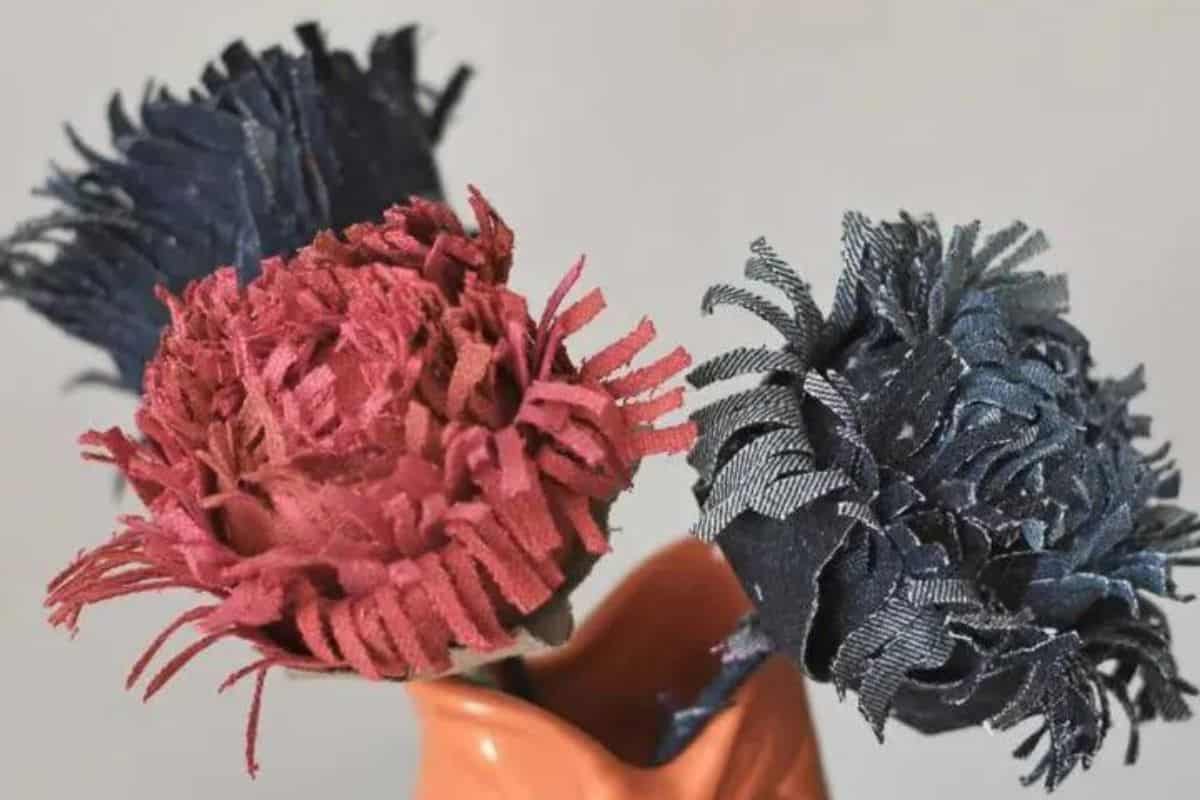 Two handmade fabric chrysanthemum-style flowers with fringed petals displayed in a small container, crafted from textured fabric strips.
