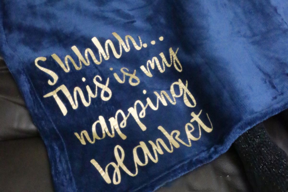 Soft navy blue blanket with gold lettering that reads "Shhhh... This is my napping blanket," draped over a surface, showcasing a cozy and relaxing vibe.