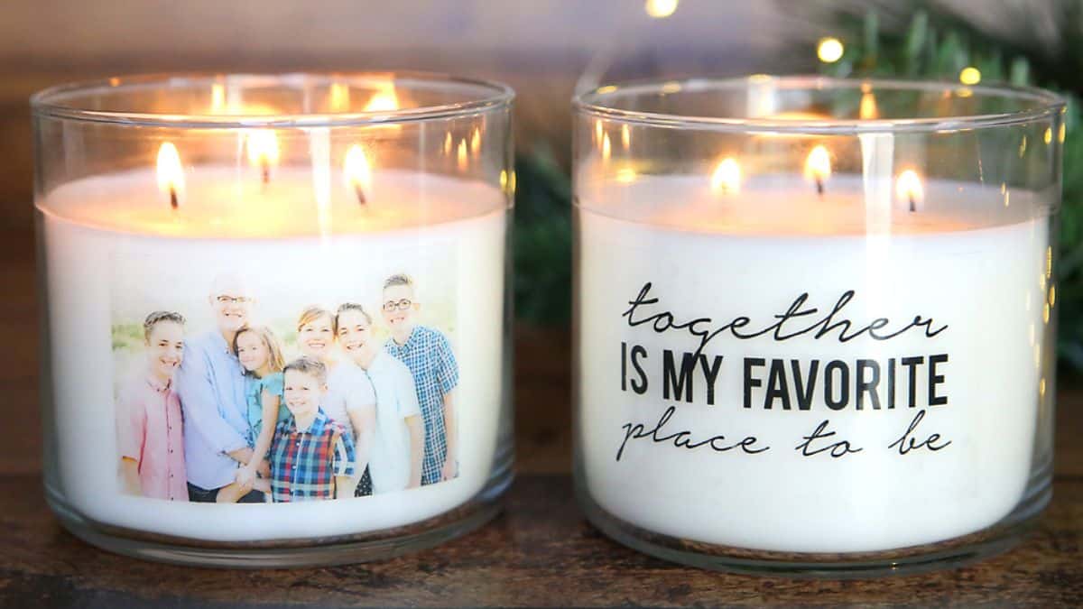 Two lit glass jar candles on a table, one personalized with a family photo and the other with a handwritten-style quote, displayed side by side.