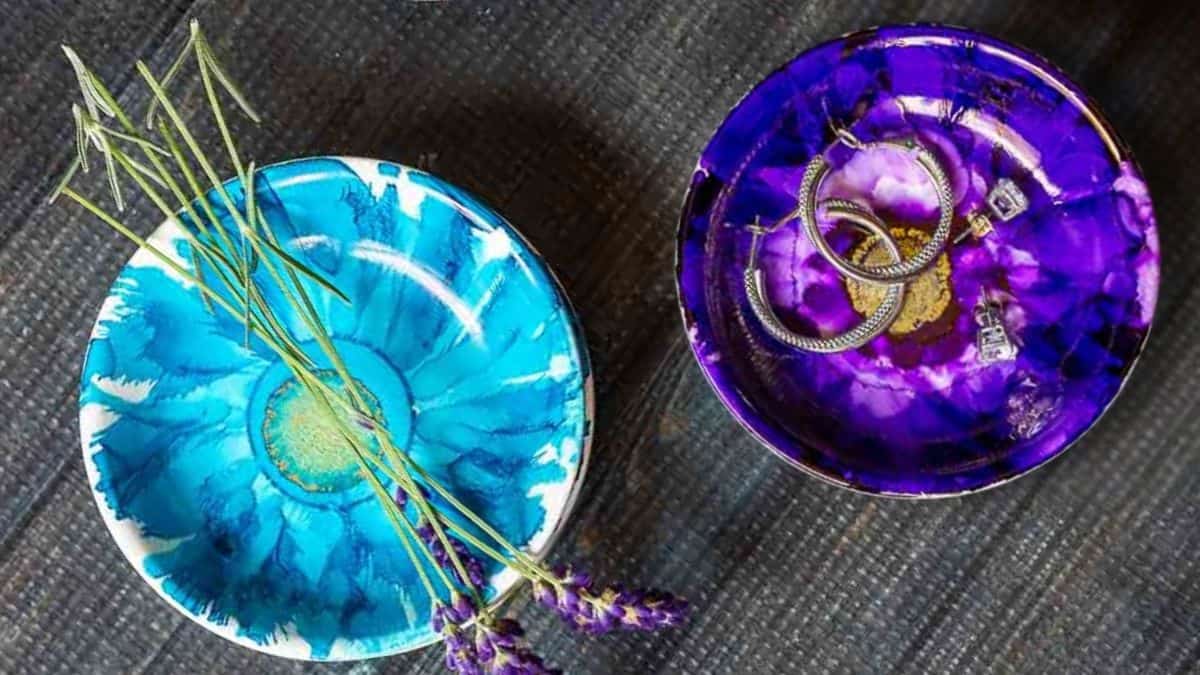 Two round handmade jewelry dishes decorated with alcohol ink designs, one holding lavender sprigs and the other holding rings and earrings.