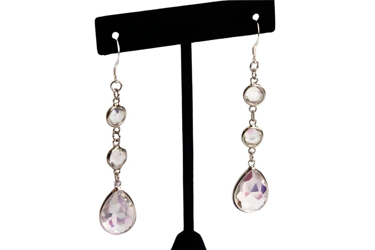 Pair of handmade dangling rhinestone earrings with clear faceted stones on silver hooks, displayed on a T-shaped earring stand.