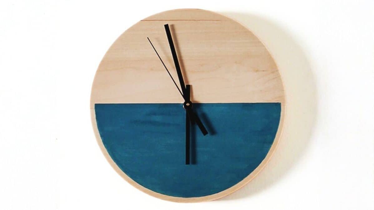 Round wooden wall clock with a painted lower half and black clock hands mounted against a plain background.
