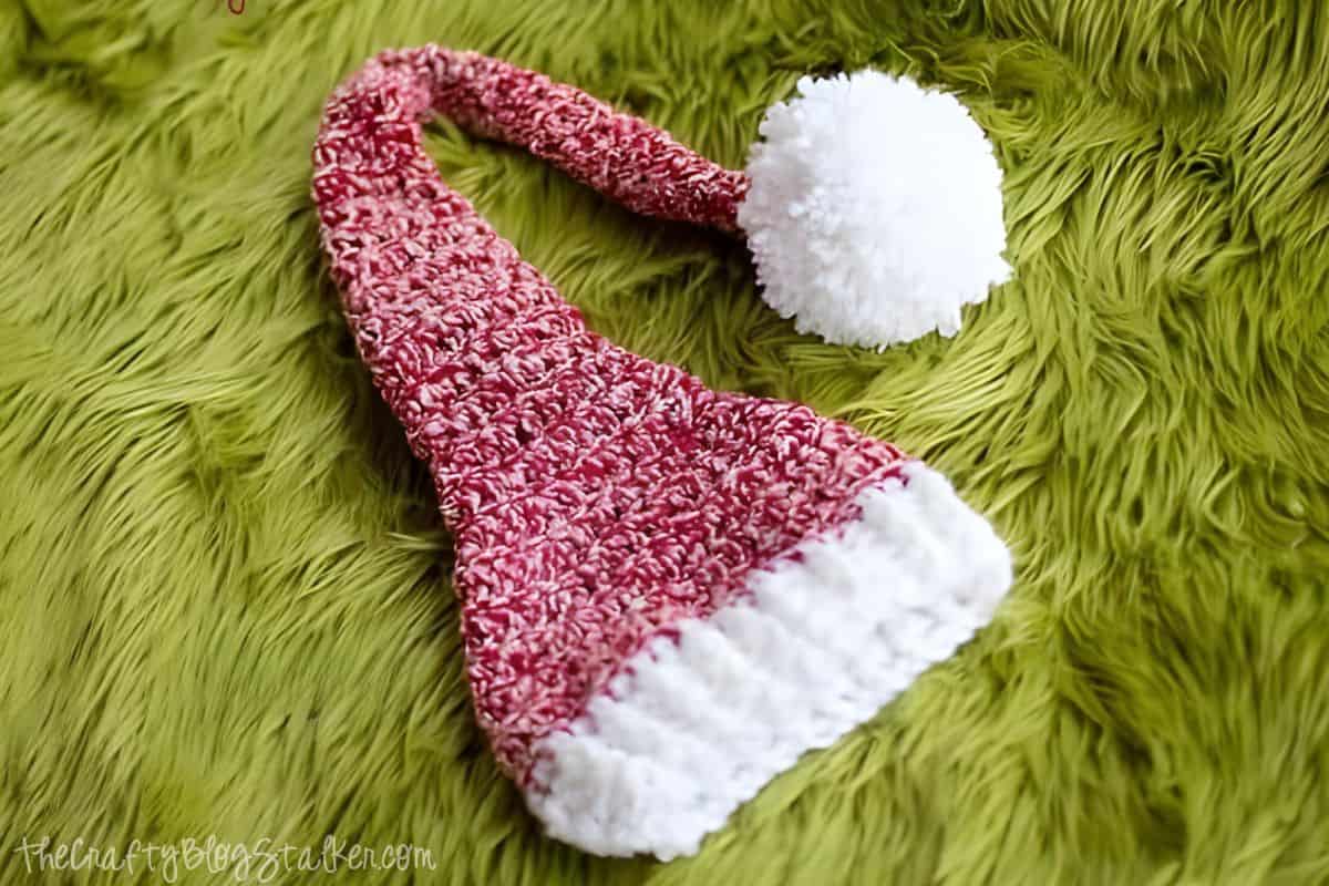 A festive red and white crochet stocking hat with a fluffy pom-pom, resting on a vibrant green textured background, perfect for cozy winter crafts or photo props.