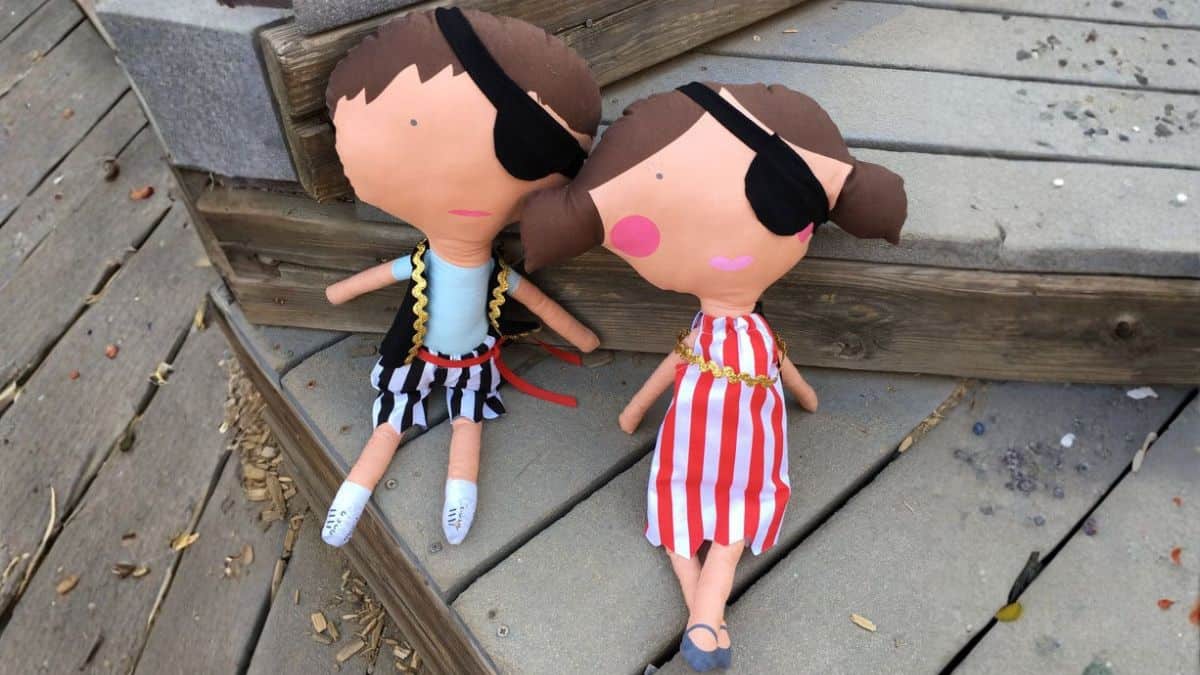 Two handmade pirate dolls with eye patches and fabric outfits sitting on outdoor wooden steps, shown side by side as part of a DIY craft project.