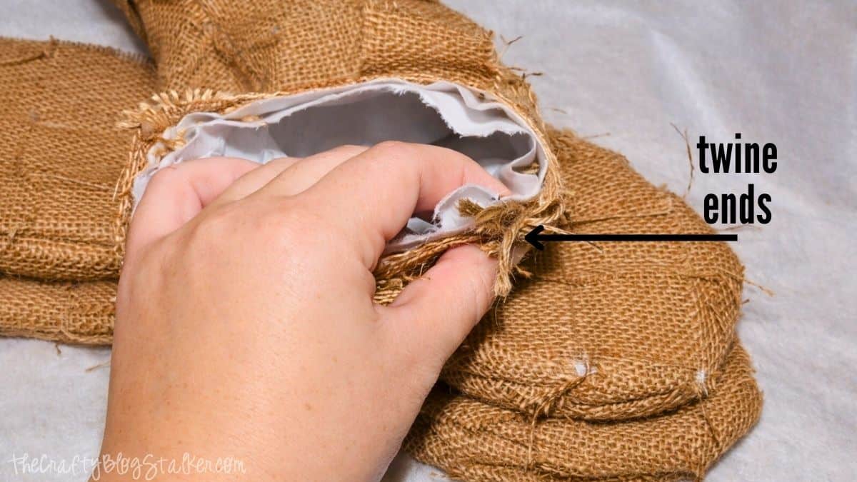 Hand holding the cuff of a burlap stocking, showing twine ends tucked inside the opening during the finishing step of a DIY woven burlap stocking.