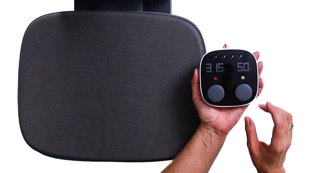 Hand holding a heat press control panel next to a heat press platen, showing temperature and time settings ready for applying iron-on vinyl.