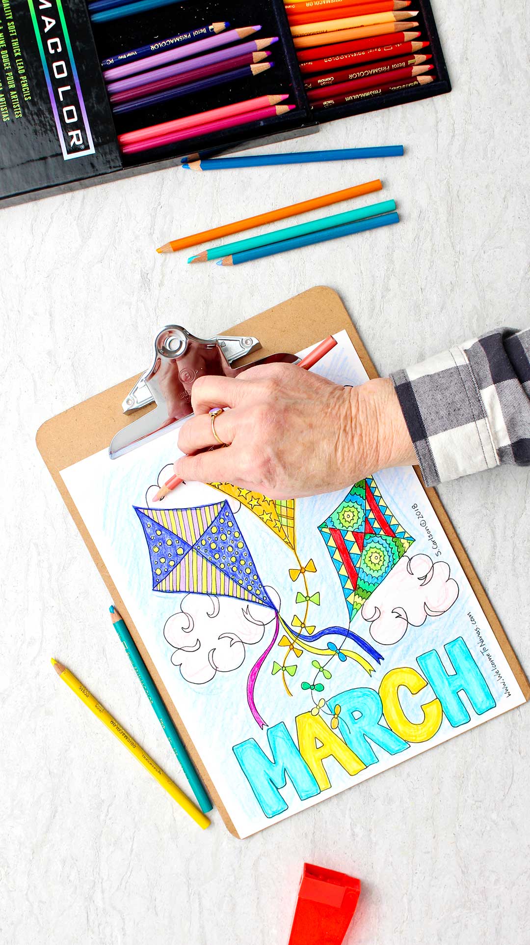 Hand using side of colored pencil to lightly shade some of the clouds on coloring page.