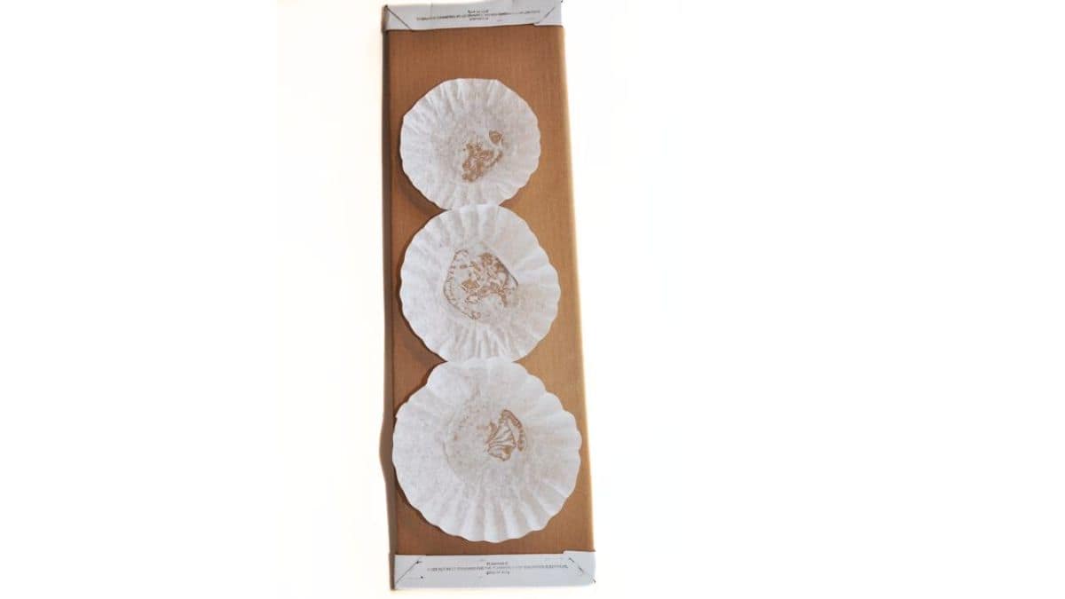 Three coffee filters glued vertically onto a brown fabric bolt, forming the base shapes for a snowman craft.