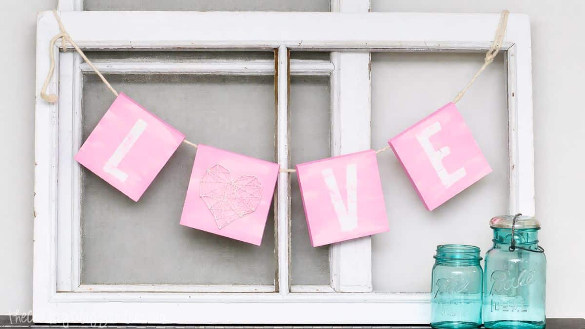 Handmade Valentine's Day banner spelling LOVE, hung across a vintage window frame with decorative mason jars on a shelf.