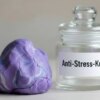 eine lilafarbene Anti-Stress-Knete liegt neben einem Glas
