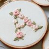 Blumenbuchstaben sticken, Stickrahmen mit Buchstabe A umgeben von Garnrollen