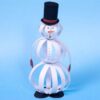 Paper strip snowman craft standing upright, made from layered paper strips with a top hat, carrot nose, and mitten hands on a plain background.